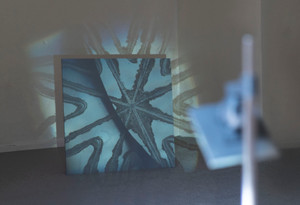 View of projection from further back, showing the room and the projection apparatus. The projection surface is in focus and the apparatus is out of focus. The room has white walls and a carpeted floor. 
