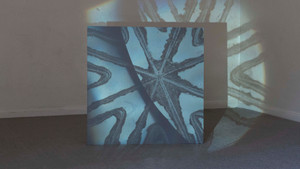 Projection of liquid on grey board. A radial pattern, slightly degraded on the edges, is visible, as well as the liquid which has areas of blue and orange.